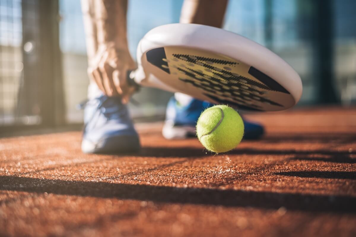Close-up of a padel racket and yellow ball above a court surface